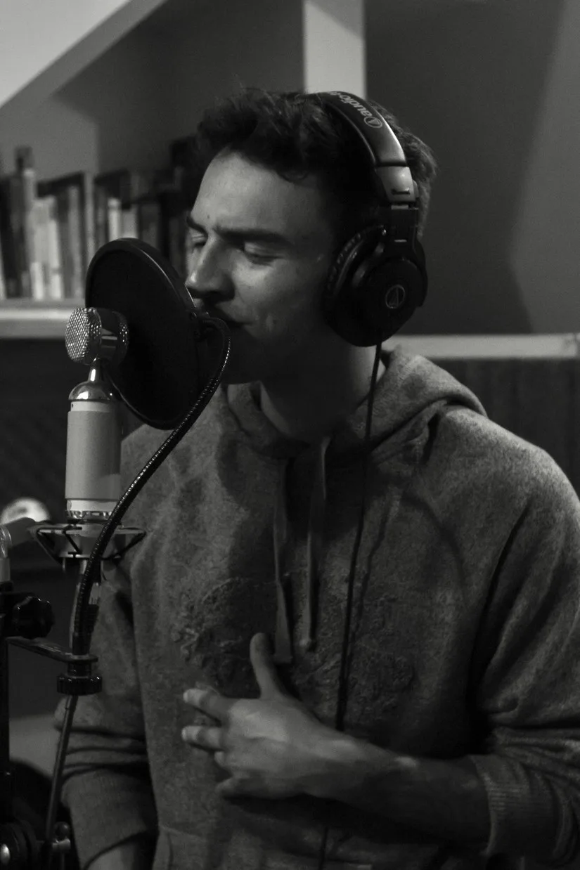 Alejandro Muñoz recording vocals in a studio, wearing headphones in front of a microphone